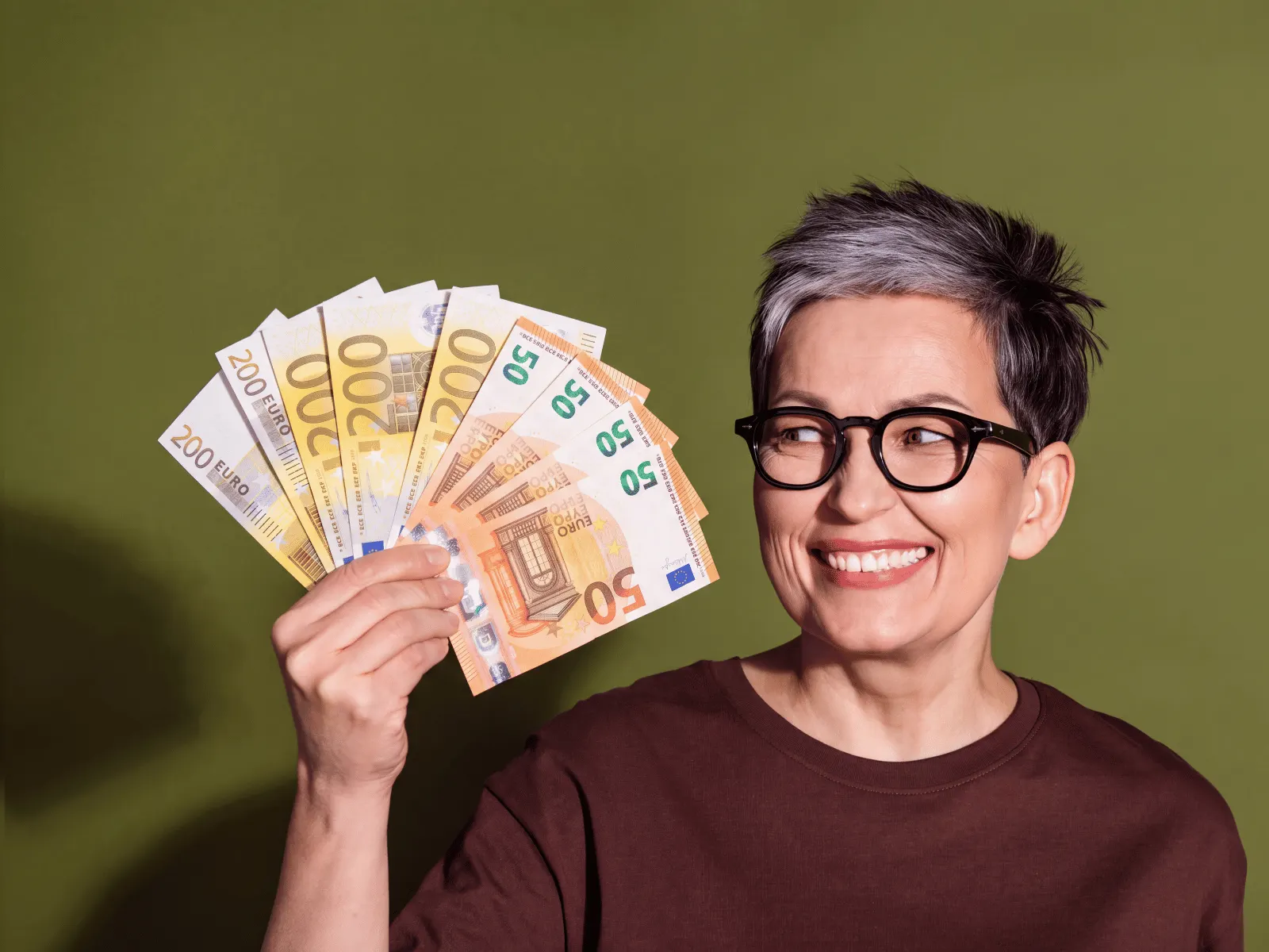 Frau mit kurzen grauen Haaren und Brille hält lächelnd einen Fächer aus Euro-Scheinen, den sie als Pfandkredit bekommen hat.